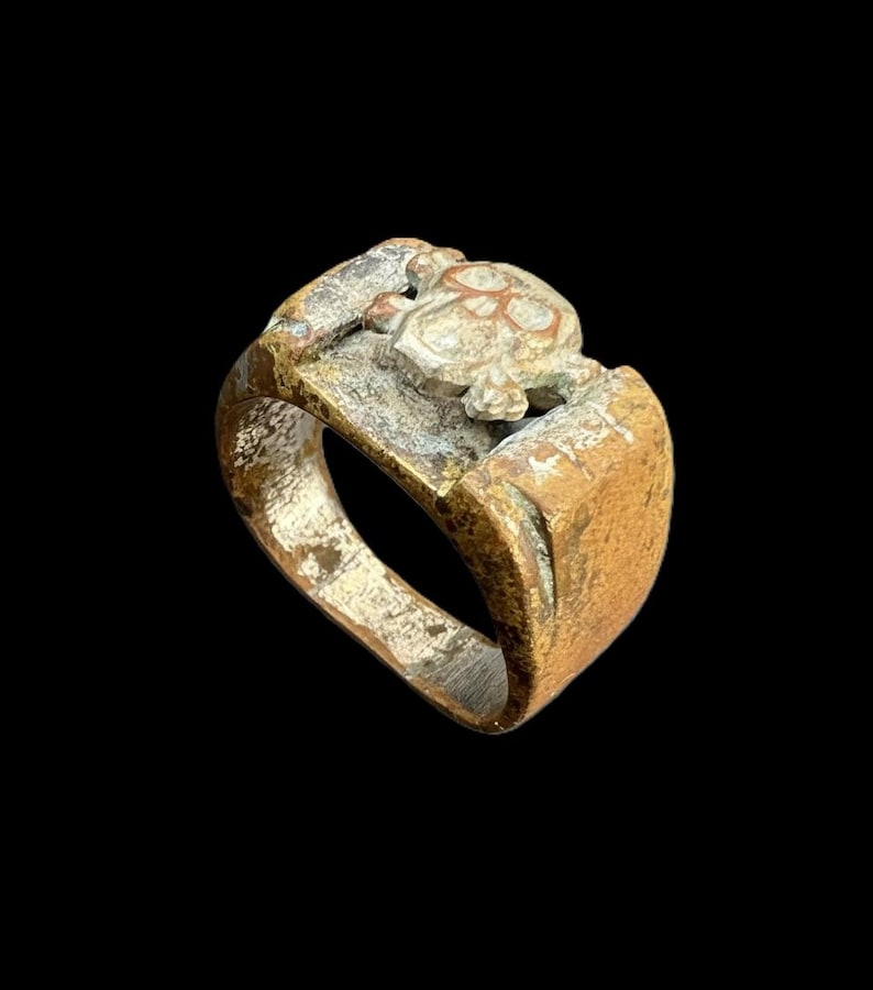 Puede incluir: Un anillo desgastado, de tono bronce, con un dise&ntilde;o de tortuga. El anillo presenta una cara rectangular con una figura de tortuga en relieve y una banda con un aspecto desgastado y texturizado. El anillo est&aacute; sobre un fondo negro.