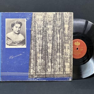 Puede incluir: Una portada de álbum de disco azul y blanco con una foto en blanco y negro de una mujer en el frente. La portada del álbum tiene un borde decorativo y el texto "H. Зашихина" está escrito en el frente. El álbum está acompañado por un disco de vinilo negro.