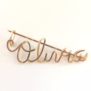 May include: Gold-toned wire brooch shaped like the word "Olivia".