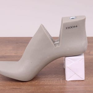 May include: A gray shoe last with a high heel and a pointed toe. The last has a number "130014" printed on the side.