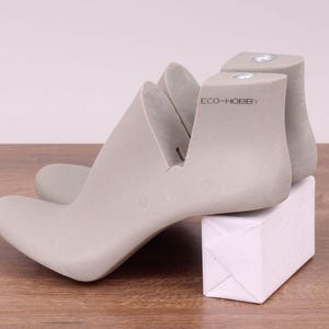 May include: A pair of gray shoe forms with a white box. The shoe forms are made of a hard plastic and have a smooth finish. The box is made of cardboard and has a white finish. The shoe forms are labeled "ECO-HOBBY".