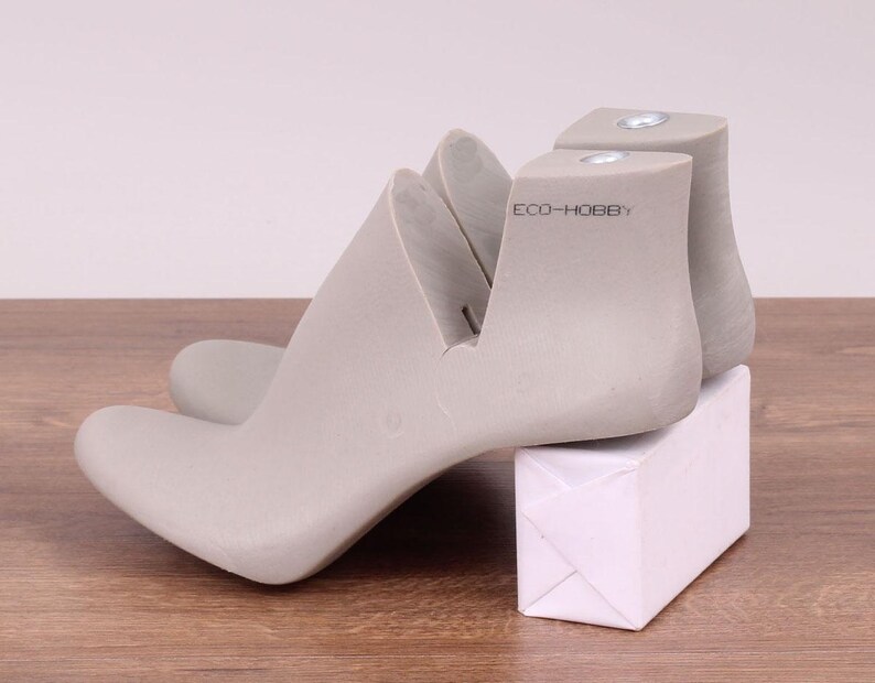 May include: A pair of gray shoe forms with a white box. The shoe forms are made of a hard plastic and have a smooth finish. The box is made of cardboard and has a white finish. The shoe forms are labeled "ECO-HOBBY".
