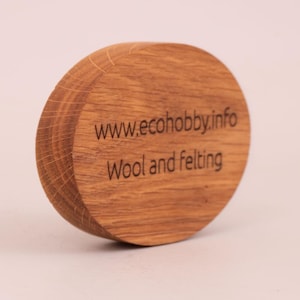 Könnte beinhalten: Eine kreisförmige Holzscheibe mit einer natürlichen hellbraunen Maserung. Auf der Vorderseite befindet sich der lasergravierte Text www.ecohobby.info, gefolgt von den Wörtern Wool and felting in einer einfachen, dunklen, serifenlosen Schrift.
