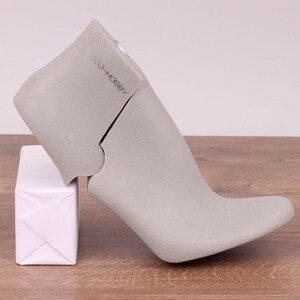 May include: A gray shoe form with a high heel and a pointed toe. The form is made of a hard plastic material and has a label that reads "CO. HOBBY". The form is sitting on a white box.