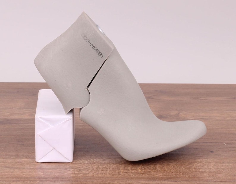 May include: A gray shoe form with a high heel and a pointed toe. The form is made of a hard plastic material and has a label that reads "CO. HOBBY". The form is sitting on a white box.