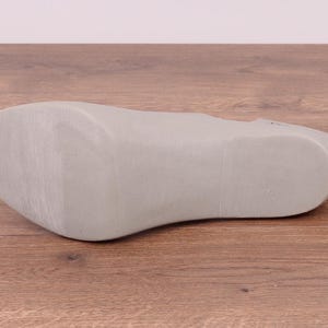 May include: The bottom of a light gray shoe with a smooth, textured sole.
