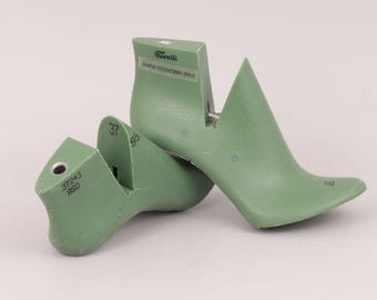 May include: Two sage green plastic shoe lasts for footwear construction. The upright piece features the text Fiorelli and WWW.ECOHOBBY.INFO. The horizontal piece is marked with 37243, RSO, and the number 37. Both pieces have a smooth finish.