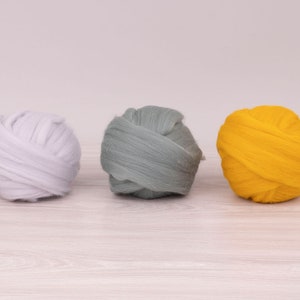 Op de afbeelding: Drie bollen wolgaren in verschillende kleuren: wit, grijs en geel.