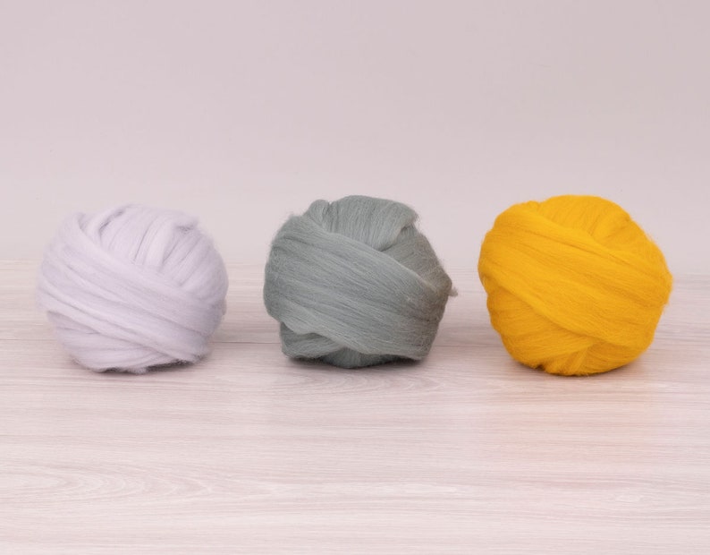 Op de afbeelding: Drie bollen wolgaren in verschillende kleuren: wit, grijs en geel.