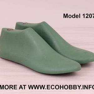 Puede incluir: Dos hormas de zapatos verdes, Modelo 12071, se muestran sobre una superficie de madera clara. Estas hormas están diseñadas para dar forma al calzado. La dirección del sitio web es visible en la parte inferior de la imagen.