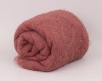May include: A rolled bundle of dusty rose colored wool roving. The fiber has a soft, fuzzy, and dense texture, coiled into a cylindrical shape. The material appears uniform in color and consistency throughout the entire rolled structure.