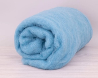 Pode incluir: Um rolo de lã cardada azul claro. A lã é macia e fofa, perfeita para feltro ou fiar.