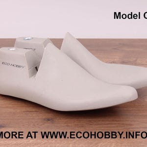 Puede incluir: Un par de hormas de zapato grises claras, Modelo C, hechas de un material liso. El texto "ECO HOBBY" está impreso en el lateral de una horma. La dirección del sitio web "MORE AT WWW.ECOHOBBY.INFO" está impresa en la parte inferior.