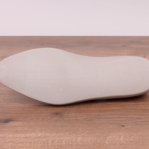 May include: A light gray shoe last, designed for shoemaking. The last is made of a solid material and has a smooth, rounded shape, with a defined heel and toe. The shoe last is approximately 11 inches long.