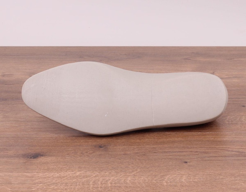 May include: A light gray shoe last, designed for shoemaking. The last is made of a solid material and has a smooth, rounded shape, with a defined heel and toe. The shoe last is approximately 11 inches long.