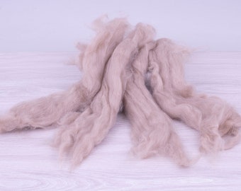 May include: A pile of light brown wool roving, a type of fiber used for spinning yarn or felting.
