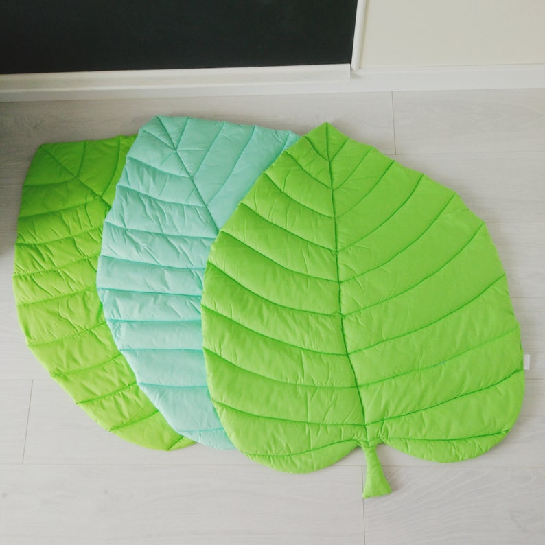May include: Three leaf-shaped play mats in green, light green, and turquoise. The mats are quilted and have a leaf vein pattern.