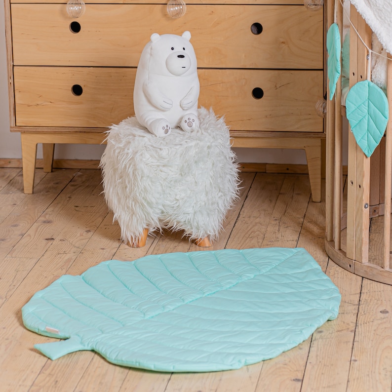 May include: A light green leaf-shaped play mat with a white polar bear plush toy sitting on a white furry stool.