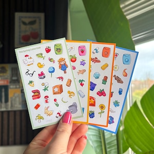 May include: Four sticker sheets with colorful spring-themed illustrations, including a chicken, fish, flowers, and a farmer. The sheets have different colored borders: green, orange, and blue. The text "The Spring Collection" is visible on the top left of the green sheet.