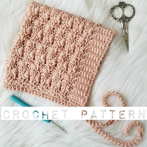 May include: A crochet pattern for a textured, pink crocheted fabric. The fabric is shown with a crochet hook and yarn.