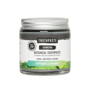 May include: A glass jar of charcoal botanical toothpaste with a silver lid. The label reads "TRUTHPASTE CHARCOAL BOTANICAL TOOTHPASTE" with "Peppermint & Spearmint" at the bottom. The toothpaste is dark grey, and the jar is on a white background.