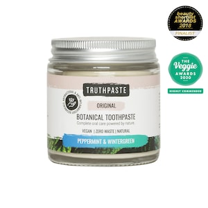 Op de afbeelding: Een glazen pot Truthpaste Botanical Tandpasta met een zilveren deksel. Het etiket bevat de tekst "Truthpaste", "Original" en "Peppermint & Wintergreen". Het product is veganistisch, zero waste en natuurlijk. Er zijn onderscheidingen zichtbaar.