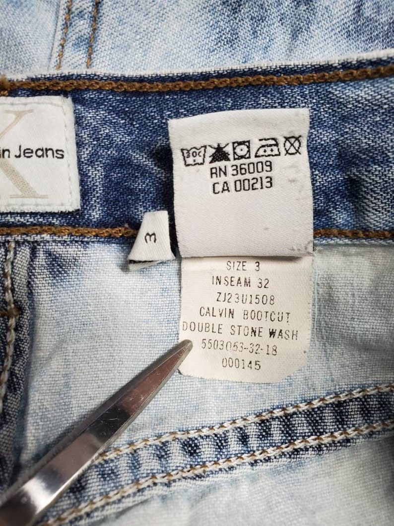 May include: A close-up of a light blue denim jean label with white text. The label reads "Size 3", "Inseam 32", "ZJ23U1508", "Calvin Bootcut", "Double Stone Wash", "5503053-32-18", and "000145".