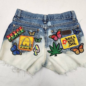 May include: Light blue denim shorts with various patches, including a peace sign, a mushroom, a marijuana leaf, a butterfly, a St. Louis arch, and a yellow patch that says "Have a Nice Day".