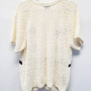 May include: A white short-sleeved sweater with black trim on the sides. The sweater is made of a soft, textured material.