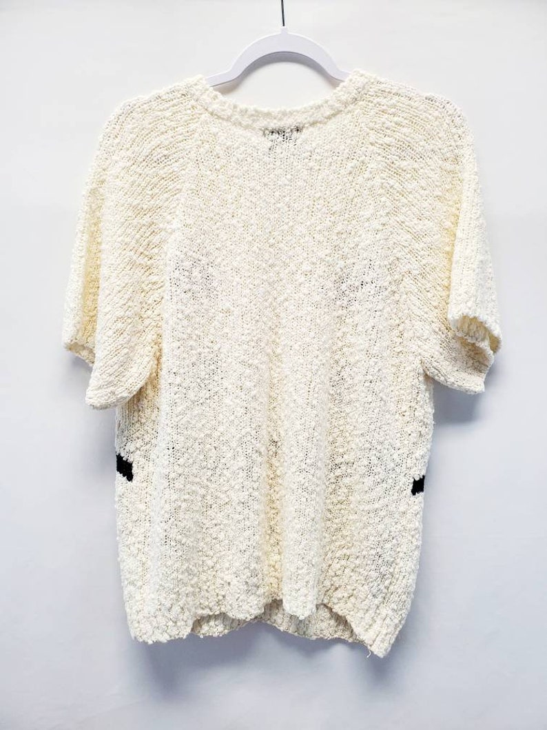 May include: A white short-sleeved sweater with black trim on the sides. The sweater is made of a soft, textured material.
