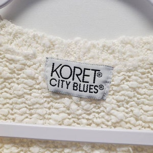 May include: White sweater with a white tag that says "Koret&reg; City Blues&reg;" in black text.