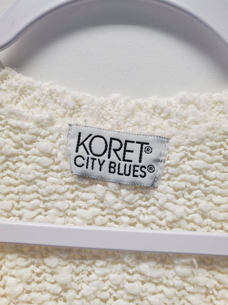 May include: White sweater with a white tag that says "Koret&reg; City Blues&reg;" in black text.