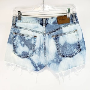 May include: Light blue denim shorts with a distressed hem and a brown leather patch that says "Calvin Klein Jeans".