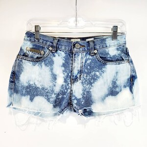 May include: Light blue denim shorts with a bleach-splattered design. The shorts have a frayed hem and a button fly.