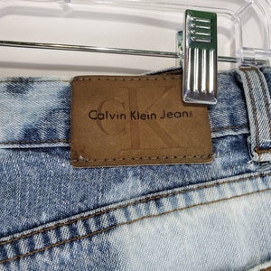 May include: A pair of light blue denim jeans with a brown leather patch that says "Calvin Klein Jeans" on the back waistband.