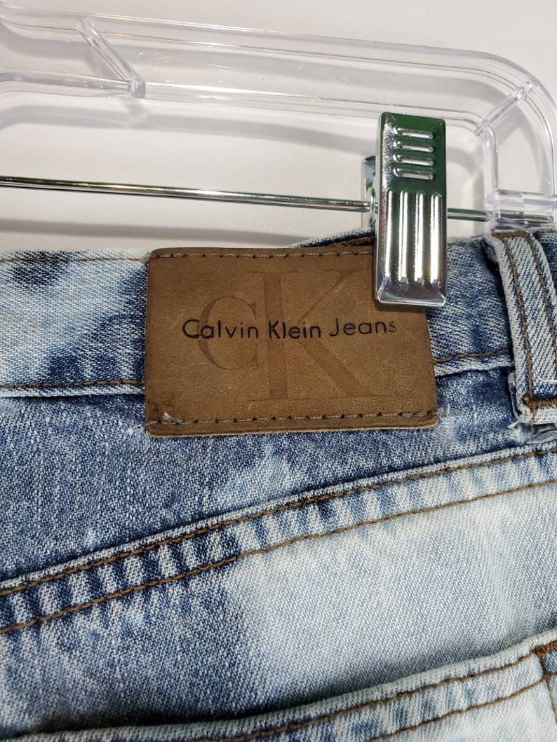 May include: A pair of light blue denim jeans with a brown leather patch that says "Calvin Klein Jeans" on the back waistband.