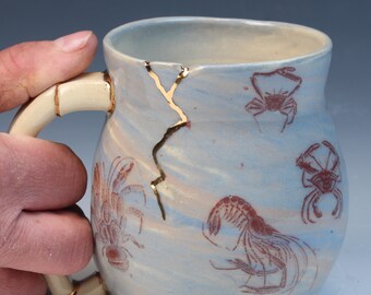 Kintsugi inspired wabi sabi functional handmade ceramic coffee or tea mug with images of crabs, shrimp,  sea shells and has real gold luster