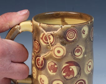 a weird kintsugi inspired yellow and brown wabi sabi functional handmade ceramic coffee or tea mug with eyes and real gold luster
