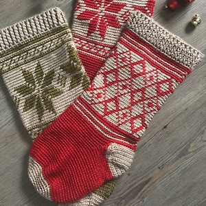 May include: Three knitted Christmas stockings with different designs. The stockings are red, green, and beige with white accents. The designs include a snowflake, a tree, and a star.
