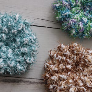 May include: Three crocheted scrubbers in different colors. One is blue and white, one is brown and white, and one is green, purple, and white.