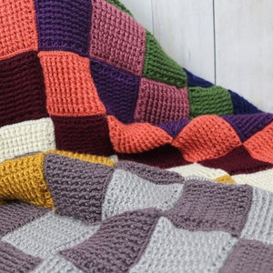 May include: A colorful crocheted blanket with squares in shades of purple, red, orange, green, yellow, gray, and white.