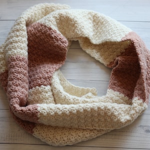 May include: A crocheted infinity scarf with alternating stripes of cream and light brown.