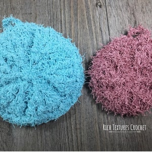 May include: Two crocheted scrubbies, one light blue and one dusty rose, on a wood background. The text "Rich Textures Crochet" is below the scrubbies.