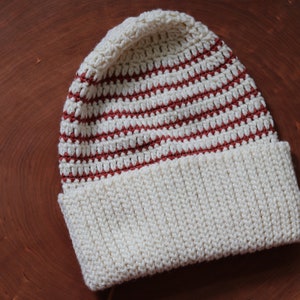 May include: A white and red striped crocheted beanie hat with a white brim.