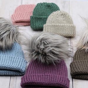 May include: Six knitted hats with faux fur pom poms in various colors, including light blue, pink, green, beige, purple, and brown.