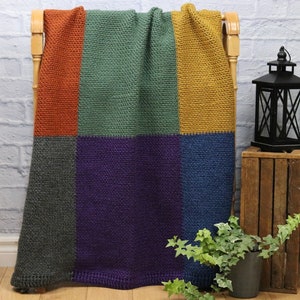 Pode incluir: Uma manta de crochê com um design de patchwork em tons de laranja, verde, cinza, roxo e azul.