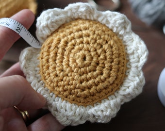 May include: A crocheted sunflower with a white center and yellow petals. The sunflower is about 2 inches in diameter.