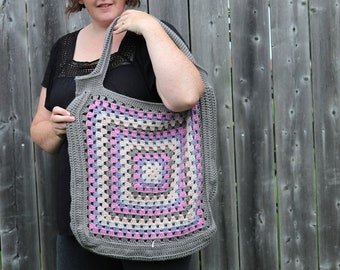 May include: A gray crocheted tote bag with a multi-colored granny square design in shades of pink, purple, and beige.