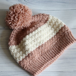 May include: A pink and white striped crocheted beanie with a fluffy pink pom pom.