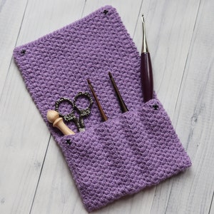 May include: A purple crocheted pouch with a flap, containing a pair of scissors, a wooden dowel, and three crochet hooks.